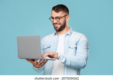 happy adult caucasian guy with glasses prints on the computer works remotely isolated on blue background. - Shutterstock ID 2075034262