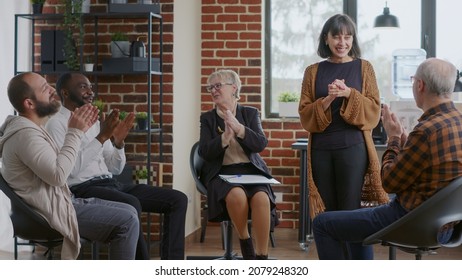 Happy Adult Celebrating Recovery Success With Group Of People Clapping Hands At Aa Meeting. Woman Sharing Achievement And Progress At Therapy, Receiving Applause From Addiction Patients.