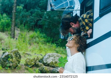 Happy adult cople have fun and love kissing outside a camper van parked in the green nature. Free parking in natural scenic place with trees. Alternative vacation and sweetness. Man and woman - Powered by Shutterstock