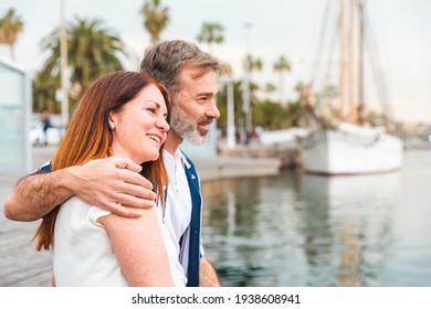 Happy adult couple relaxing on the pier in Barcelona - Man and woman together on a summer sunny day in Barcelona, hugging and looking at boats - Love and lifestyle concepts