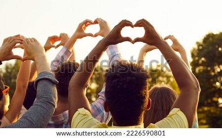 Happy adult diverse multiethnic people raise hands up in air, do heart shaped gestures, share good vibes, hope for peaceful future, send kind wishes to universe. Outdoor outside back view group shot