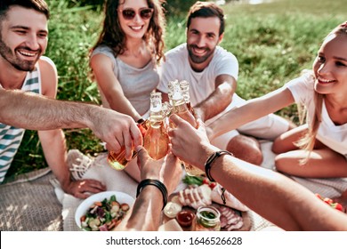 Happy Adult Friends Cheering With Beers At Picnic Outdoor. Group Of People Having Fun Eating At A Picnic. Summer Lifestyle, Friendship And Food Concept. Focus On Close-up Hands Beer