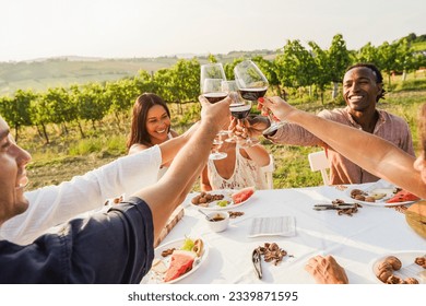 Happy adult friends having fun drinking red wine and eating together with vineyard in background - Multiracial people doing appetizer at summer time in countryside resort - Main focus on hands - Shutterstock ID 2339871595