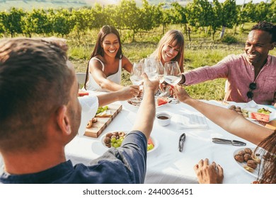 Happy adult friends having fun cheering with white wine and eating together - Multiracial people doing party at summer time in countryside resort with vineyard in background - Focus on bottom hands
 - Powered by Shutterstock