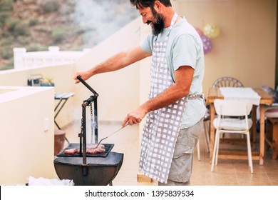 Happy Adult Man With Beard Cooking Meat With Grill Barbecue At Home For Friends To Have Fun Together - Real Life Scene Of People House Lifestyle With Bbq And Food