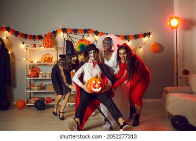 Happy Adult People Dressed Up As Evil Characters Having Fun At Crazy Halloween Horror Party At Home. Group Of Girls And Their Friend In Vampire Costume Fooling Around, Having Fun And Laughing Together