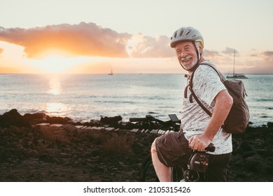 Happy adult senior cyclist man stops at the beach at sunset light enjoying freedom and beauty in nature. Elderly man with protective helmet and backpack. Copy space - Powered by Shutterstock