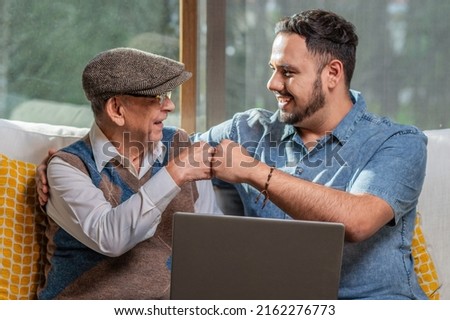 Happy adult senior father with his adult son. Young man enjoys teaching his older father how to use a laptop. How to use technology.