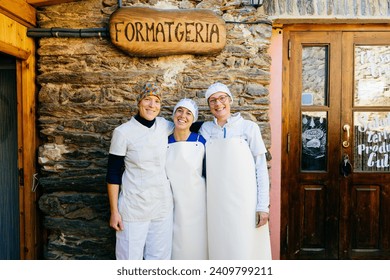 Happy adult smiling female workers in white uniforms embracing each other against entrance of cheese shop with Formatgeria signboard - Powered by Shutterstock