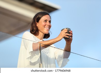 Happy adult woman with coffee cup looking away on a hotel balcony on vacation at summer - Powered by Shutterstock