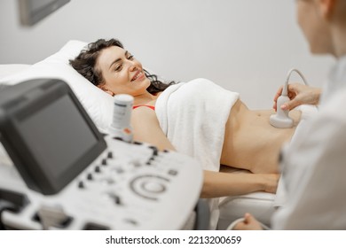 Happy adult woman during an ultrasound examination of the abdominal cavity at modern medical office. Concept of women's health and examination during pregnancy - Powered by Shutterstock