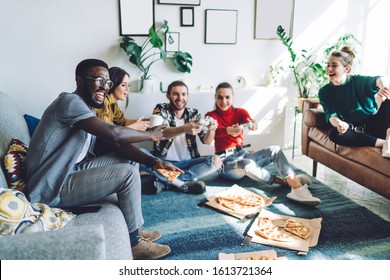 Happy Adult Woman  Pointing Finger On Screen And Looking At African American Man With Pizza Snack While Worrying With Surprised Lady Sitting On Sofa About Friends Playing Video Game During Home Party