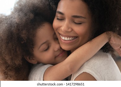 Happy Affectionate African Family Mom And Cute Little Child Daughter Embrace With Eyes Closed, Smiling Foster Parent Mother And Small Kid Girl Hugging Cuddling Enjoy Tender Warm Moment, Close Up View