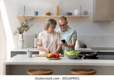 Happy affectionate middle aged mature retired married couple enjoying cooking meal together, checking recipes in cellphone application, preparing fresh vegetarian healthy food on weekend in kitchen. - Powered by Shutterstock