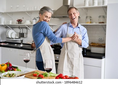 Happy affectionate older middle aged couple laughing, dancing, preparing healthy meal in modern kitchen apartment. Senior husband and wife enjoying dance having fun celebrating Valentines day at home. - Shutterstock ID 1896484612