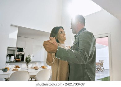 Happy affectionate romantic middle aged mature couple dancing at home. Smiling senior older man and woman in love standing in house kitchen enjoying dance lit with sunlight. Authentic photo. - Powered by Shutterstock