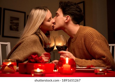 Happy Affectionate Young Couple In Love Kissing, Drinking Red Wine Having Romantic Dinner Date Celebrating Valentines Day On February 14 Or Anniversary Sitting At Table At Home Or In Restaurant.