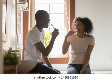 Happy african 30s spouses sit in modern light bathroom cleaning teeth enjoy each moment together, couple in love holding toothbrush brushing tooth, morning routine lifestyle healthcare hygiene concept - Powered by Shutterstock