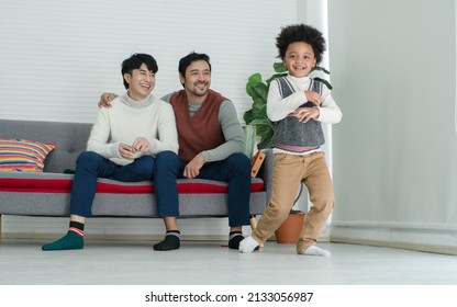 Happy African Adopted Kid Boy Wearing Sweater Dancing Hip Hop In Front Of Asian Young Gay Parent Looking With Pride Face At Living Room At Home. Lgbt Family Supporting Dream Of Their Son