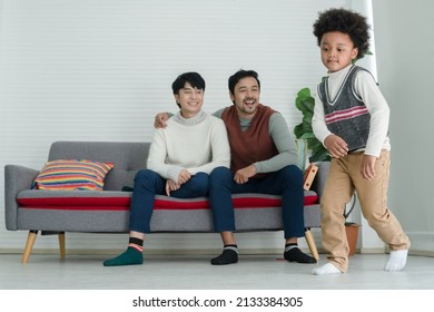 Happy African Adopted Kid Boy Wearing Sweater Dancing Hip Hop In Front Of Asian Young Gay Parent Looking With Pride Face At Living Room At Home. Lgbt Family Supporting Dream Of Their Son