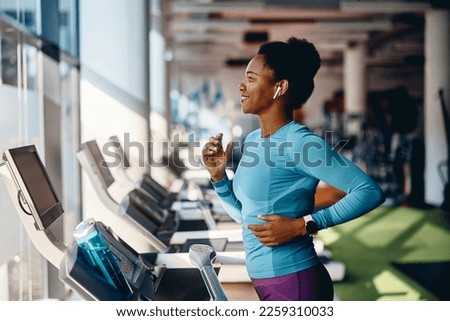 Happy African American athlete jogging on treadmill during her sports training in a gym.