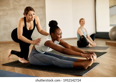 Happy African American athletic woman stretching her body while female instructor is assisting her. - Powered by Shutterstock