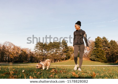Happy African American athletic woman enjoying while walking her dog in nature. 