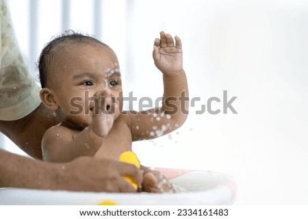 Happy African American baby girl bathing in bathtub, playing and smiling, cleaning the body for good health