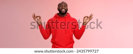 Happy african american bearded man in red hoodie meditating found peace nirvana smiling delighted close eyes relaxed relieved standing lotus mudra pose search zen, practice yoga, pink background.