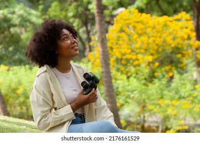 happy african american beautiful woman holding binoculars In a park with many trees. Birdwatching. Birdwatching. Look for something with binoculars.