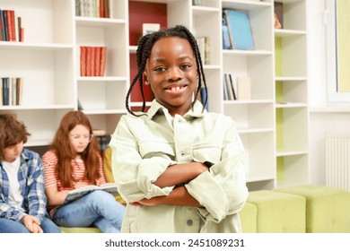 Happy African American boy looking at camera while posing in the library with his classmates reading book on the background - Powered by Shutterstock