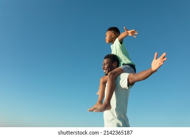 Happy african american boy on father's shoulders by copy space against clear blue sky. unaltered, family, lifestyle, togetherness, enjoyment and holiday concept. - Powered by Shutterstock