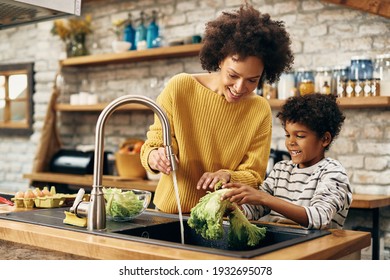 Happy African American Boy With  Other Washing Salad While Preparing Food In The Kitchen. 