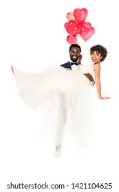 happy african american bridegroom holding in arms bride in wedding dress with balloons  isolated on white 
