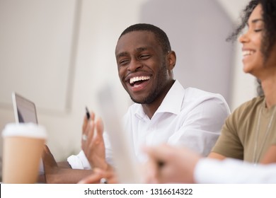 Happy african american businessman laughing talking working together with friendly colleagues, smiling millennial black man having fun team conversation joking with coworkers during office break