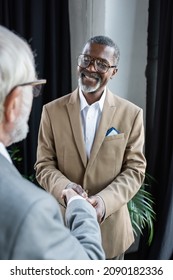 happy african american businessman shaking hands with senior business partner on blurred foreground