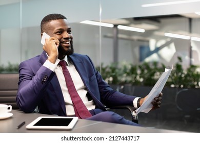 Happy african american businessman sitting at workdesk with modern digital tablet with blank screen on at office, having phone call with business partner, holding papers, panorama with copy space - Powered by Shutterstock