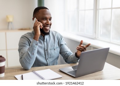 Happy African American Businessman Talking On Mobile Phone Sitting At Workplace Indoors. Office Worker Chatting By Cellphone Having Business Call Conversation. Communication Concept