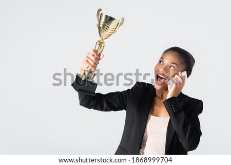 happy african american businesswoman with golden cup talking on smartphone isolated on grey
