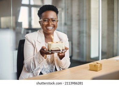 Happy African American businesswoman holding cake with lightened candle in the office and looking at camera. 