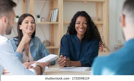 Happy african american businesswoman telling employees about project sit at table in coworking boardroom at meeting. Smiling laughing diverse female leader discuss business strategy colleagues.