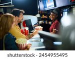 Happy African American cahier selling drinks and popcorn to a couple in cinema.