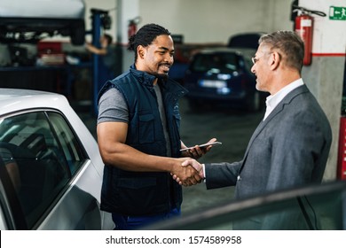 Happy African American Car Repairman Greeting With Male Customer In Auto Repair Shop. 