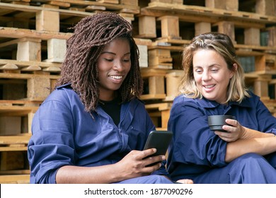 Happy African American and Caucasian factory colleagues in overalls watching content on cellphone together while drinking coffee in warehouse. Labor or communication concept - Powered by Shutterstock