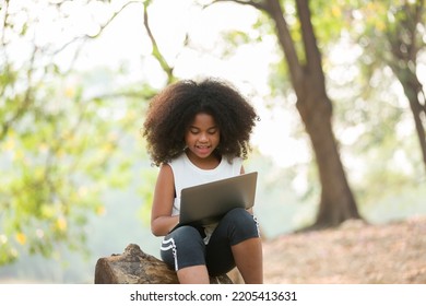 Happy African American Child Girl Using Laptop Computer Outdoors In The Park. Kid Girl Learning Outside At The School