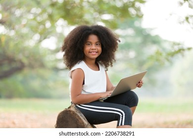 Happy African American Child Girl Using Laptop Computer Outdoors In The Park. Kid Girl Learning Outside At The School