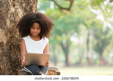 Happy African American Child Girl Using Laptop Computer Outdoors In The Park. Kid Girl Learning Outside At The School