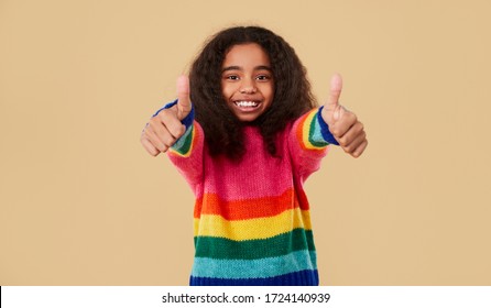 Happy African American Child In Rainbow Sweater Smiling For Camera And Showing Thumbs Up Against Beige Background