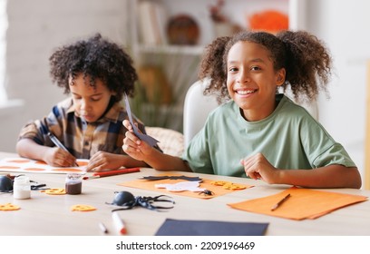 Happy African American Children Girl And Boy Making Halloween Home Decorations Together, Kids Painting Pumpkins And Making Paper Cuttings