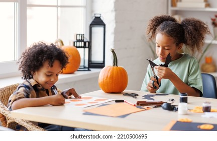 Happy African American Children Girl And Boy Making Halloween Home Decorations Together, Kids Painting Pumpkins And Making Paper Cuttings